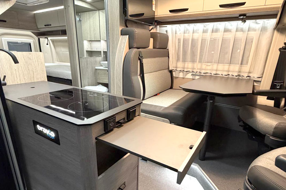 Innenaufnahem vom Bravia Van mit Sitzgelegenheit, Tisch, drehbarer Fahrersessel, Fernseher, Küchenzeile mit Dekoelementen und der Blick nach hinten aufs Heckbett mit hinteren Aussetntüre und zwei fenstern